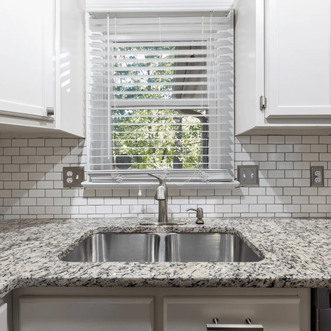 White faux wood blinds over a kitchen sink window in an Orange County home
