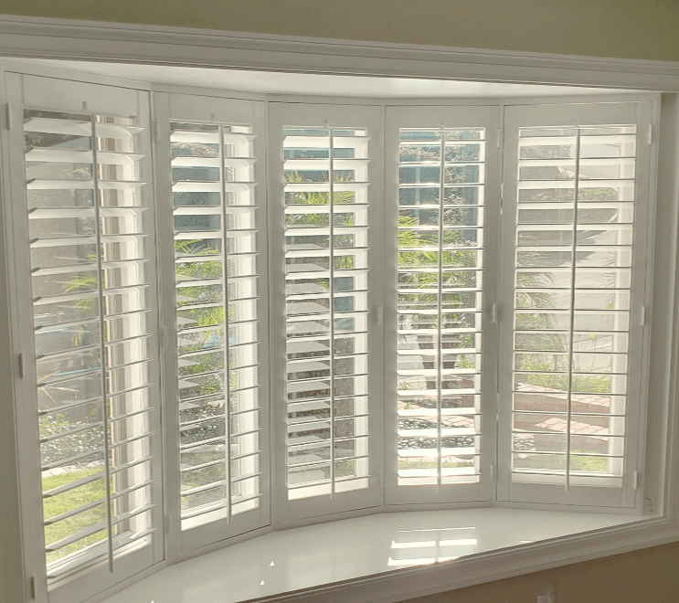 Custom white bay window shutters with wide louvers, fitted to a curved interior bay