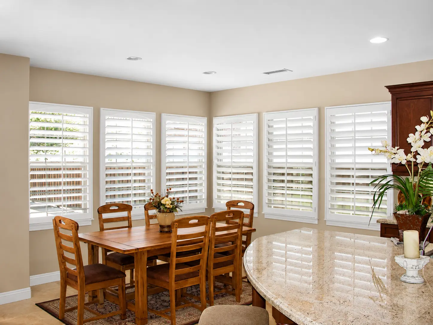 White plantation shutters across six windows in a traditional kitchen-dining area