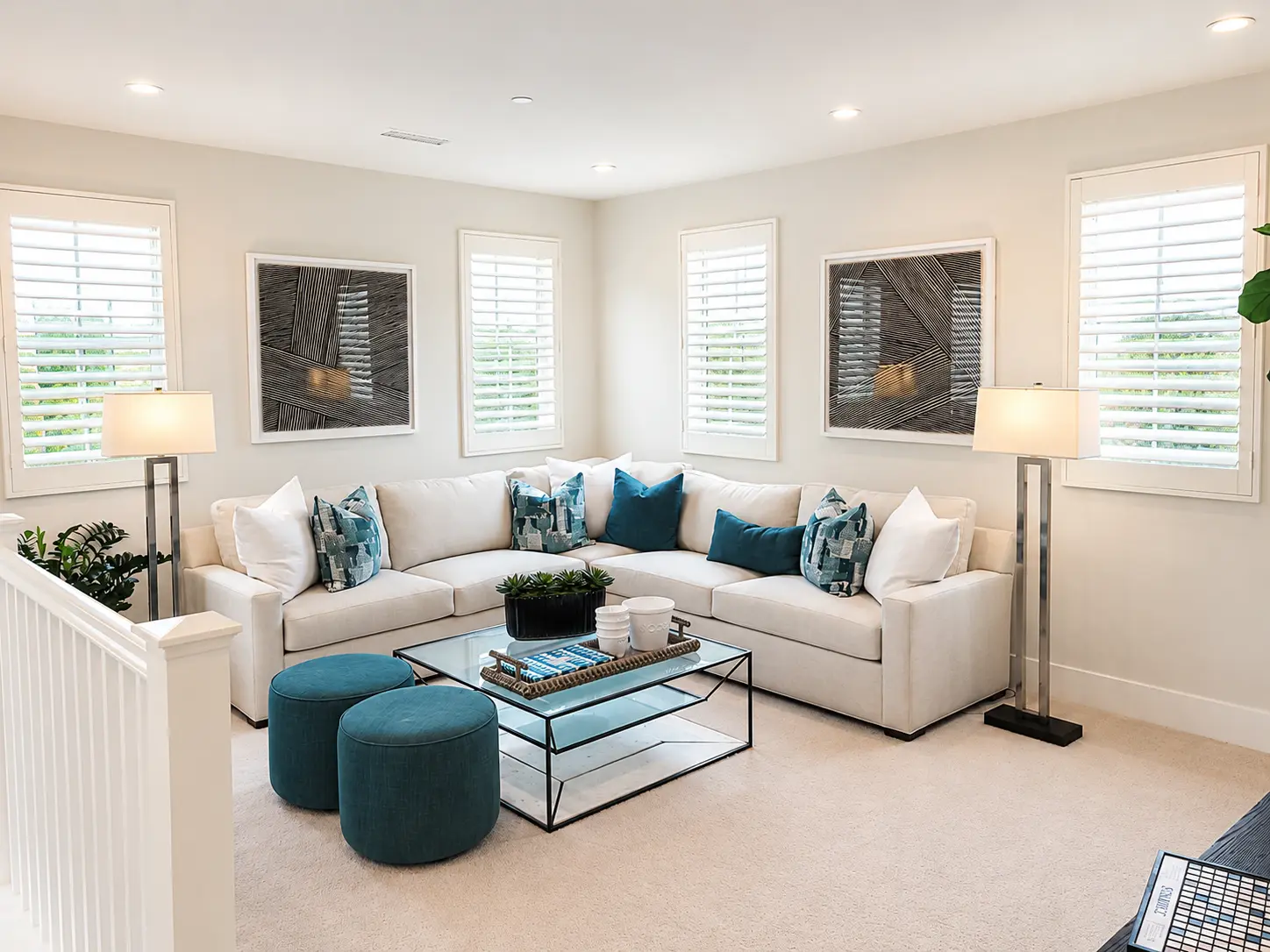 White plantation shutters on small windows above sectional in a teal-accented loft