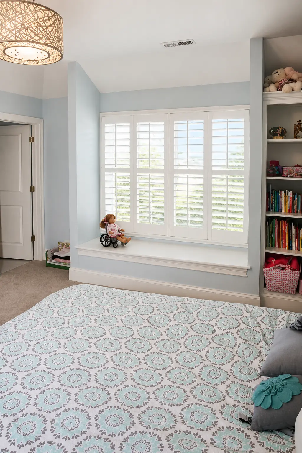 White plantation shutters on a small window above a built-in bench seat in a girl's bedroom