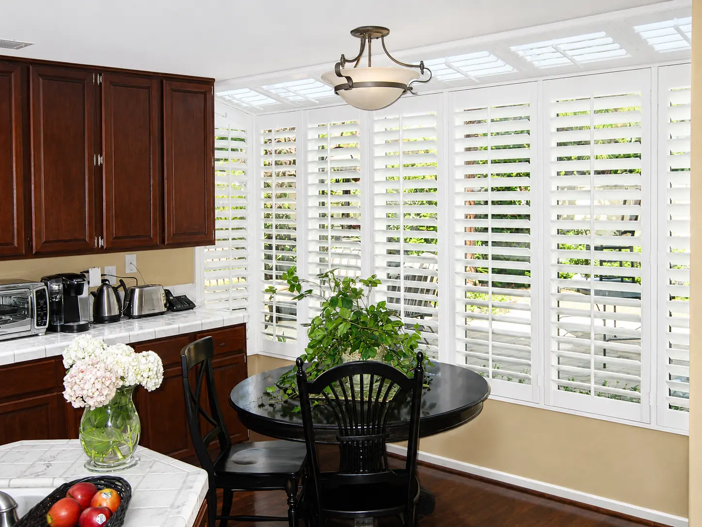 White plantation shutters across a wide kitchen window over a breakfast nook