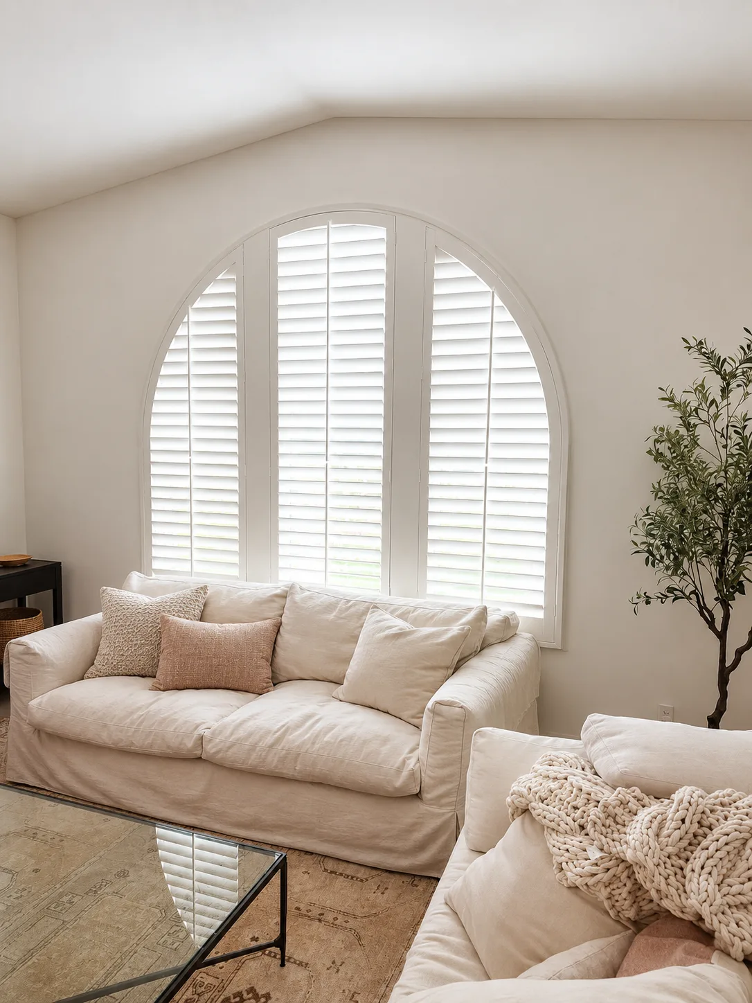 White arched-top plantation shutter above a cream sofa in a neutral living room