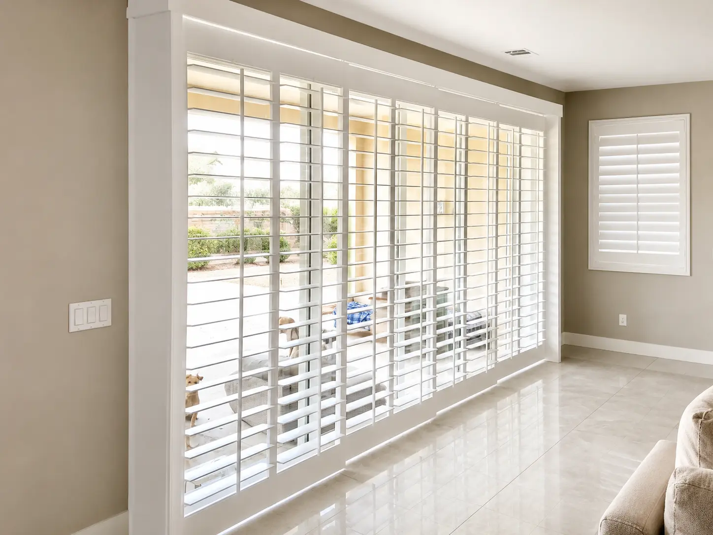White plantation shutters with track system across a wide patio slider