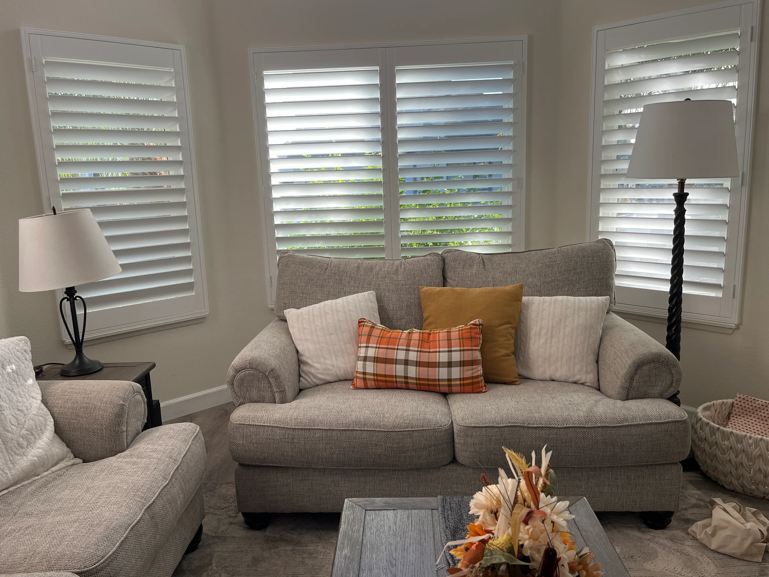 White plantation shutters on a bay window above a cozy living-room sofa