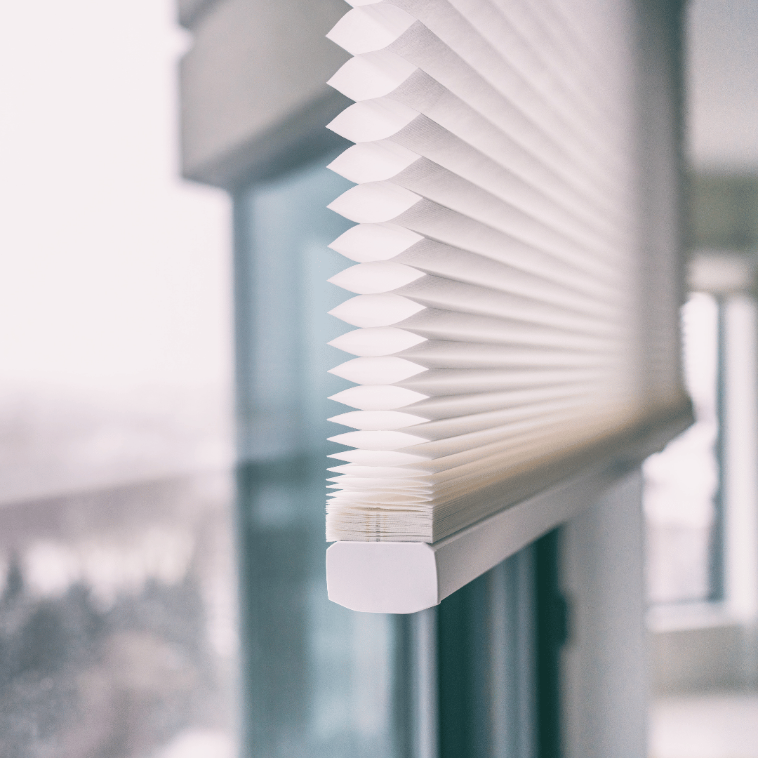 Close-up of a white honeycomb cellular shade raised beside a bright window