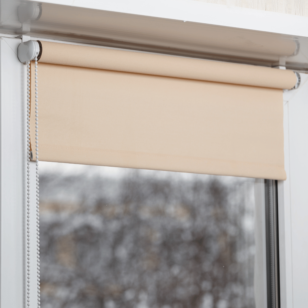 Beige roller shade partially lowered over a window on a cool winter day